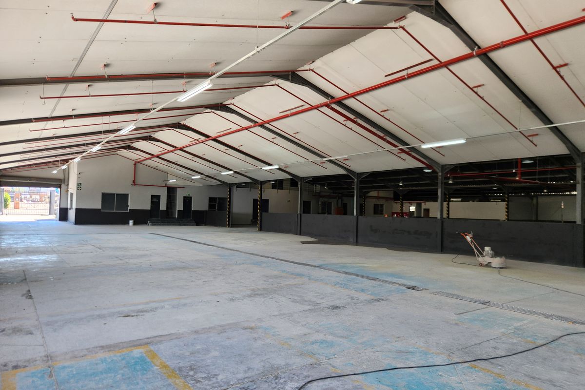Spacious industrial warehouse featuring high ceilings with exposed steel trusses, fire sprinkler system, and durable concrete flooring, suitable for various commercial or storage operations.