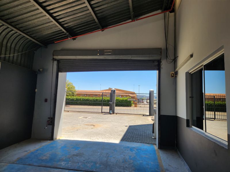 Industrial garage space featuring a large roller shutter door, metal roofing, and direct access to a paved exterior yard area.