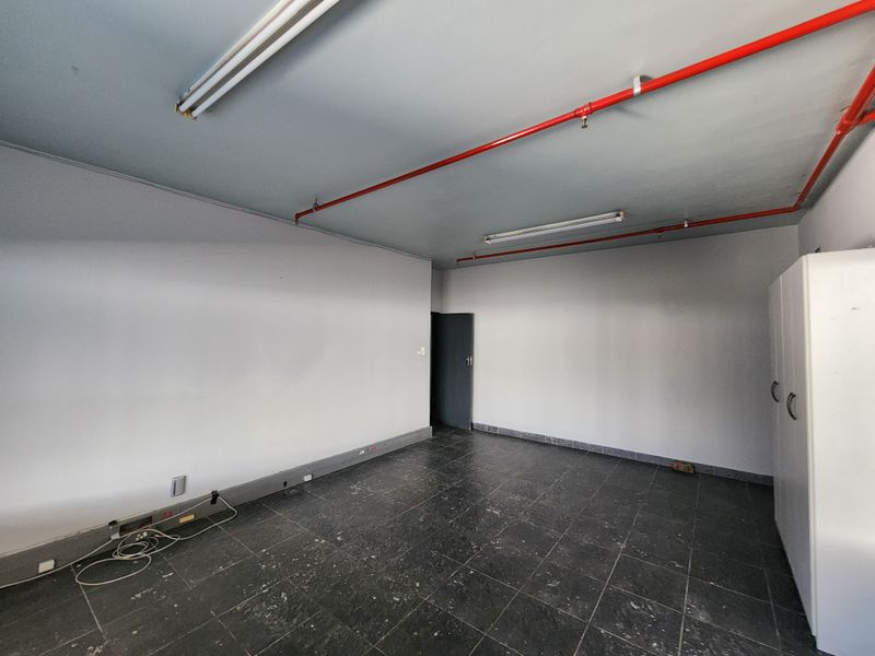 An empty industrial utility space featuring exposed red fire sprinkler piping, fluorescent lighting, and dark tiled flooring.