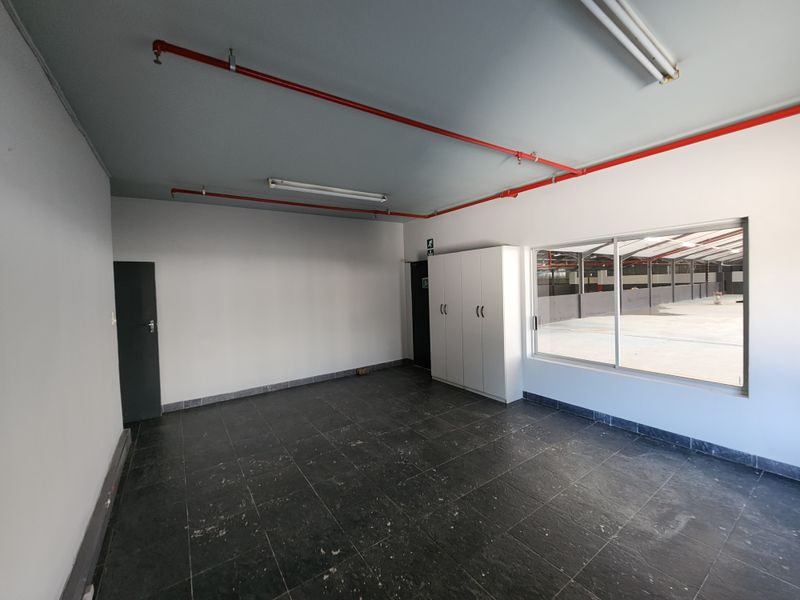 A clean, empty office space featuring tiled flooring, built-in storage cabinetry, and an integrated fire sprinkler system with a view into the warehouse area.