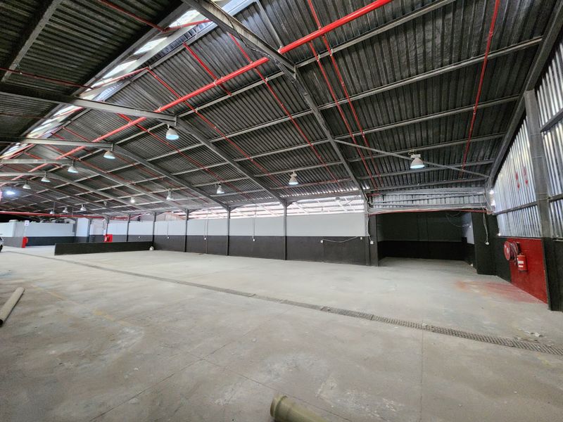 Spacious industrial warehouse unit featuring high ceilings with exposed steel trusses, fire sprinkler system, durable concrete flooring, and integrated industrial lighting.