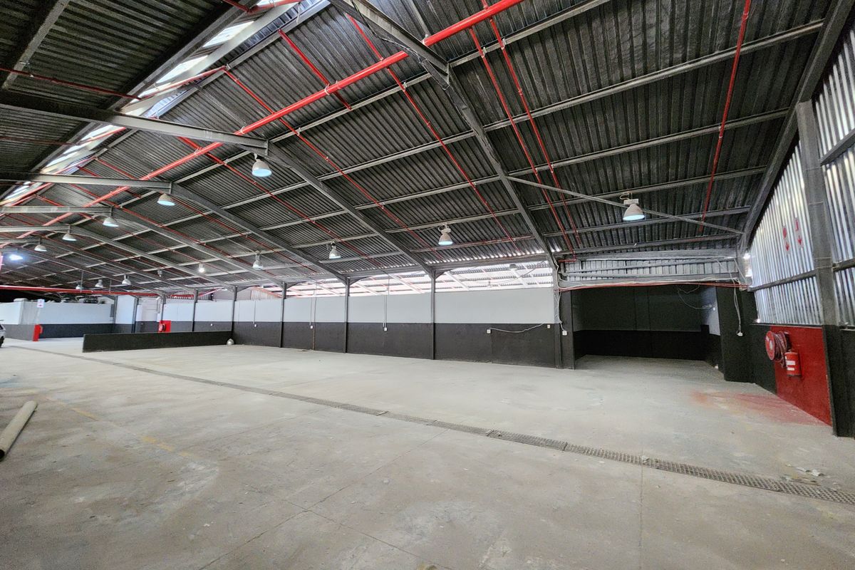 Spacious industrial warehouse unit featuring high ceilings with exposed steel trusses, fire sprinkler system, durable concrete flooring, and integrated industrial lighting.