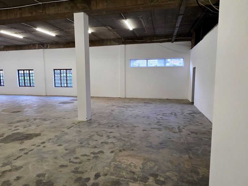 Spacious industrial utility area featuring exposed concrete ceilings, support columns, and large grid-pattern windows, offering a versatile open-plan layout.
