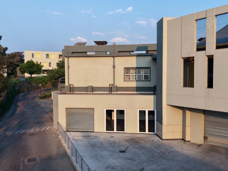Rear exterior view of the industrial property featuring concrete driveway access, roller shutter doors, and double glass entry doors.