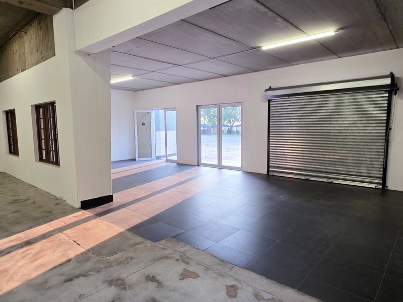 Spacious industrial utility area featuring a roller shutter door, tiled flooring, and ample natural light through glass panel doors.
