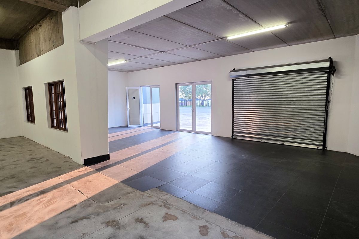 Spacious industrial utility area featuring a roller shutter door, tiled flooring, and ample natural light through glass panel doors.