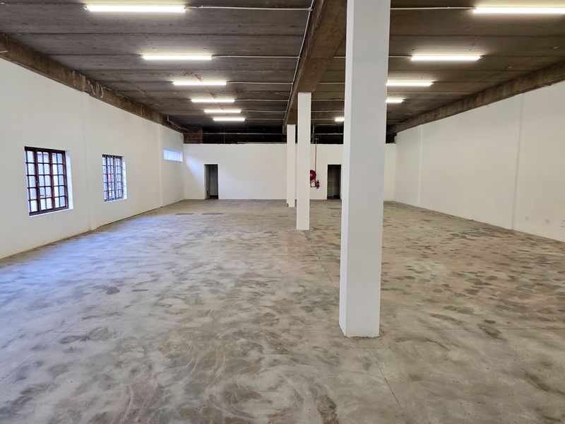 Spacious open-plan industrial unit featuring high exposed concrete ceilings, structural support columns, polished concrete flooring, and multiple grid-pattern windows providing natural light.