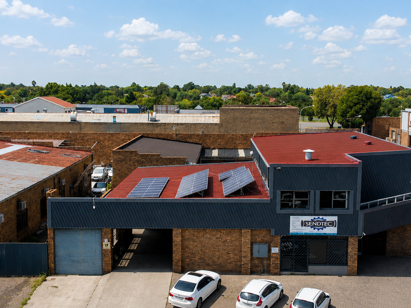 Aerial view of a commercial property featuring a brick facade, metal roofing with installed solar panels, and an adjacent paved parking area.