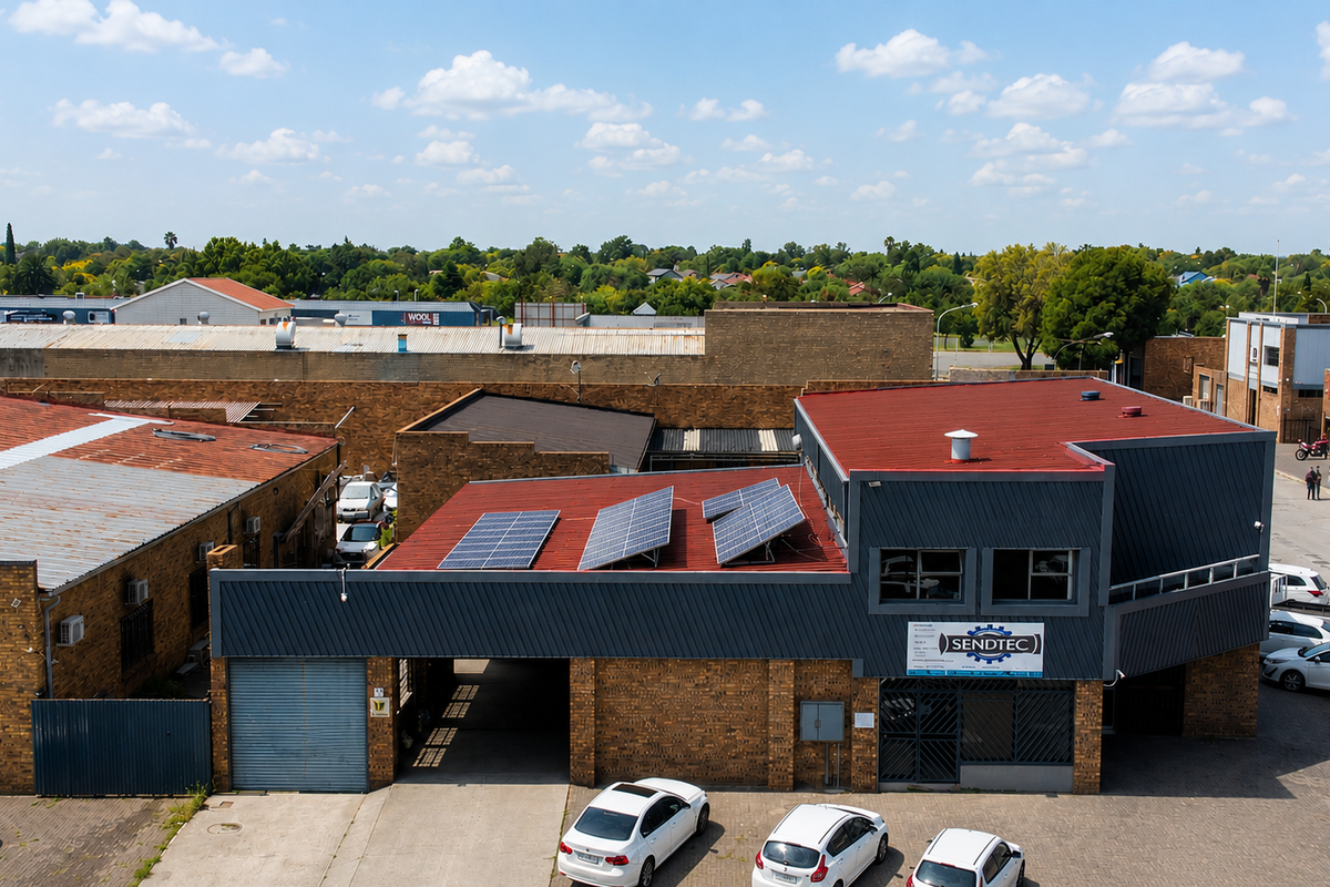 Aerial view of a commercial property featuring a brick facade, metal roofing with installed solar panels, and an adjacent paved parking area.
