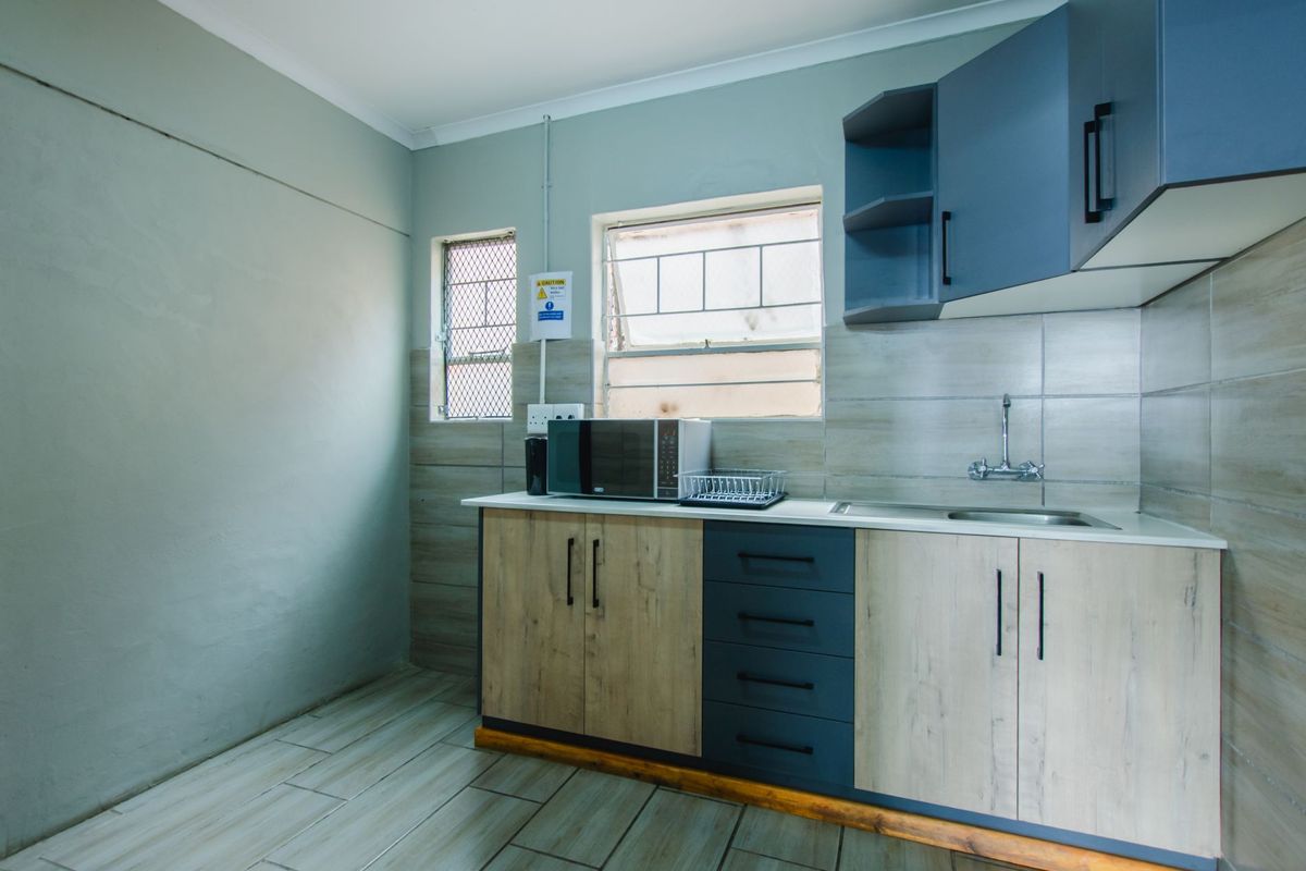 Compact kitchen area featuring modern two-tone cabinetry, tiled backsplash, stainless steel sink, and tiled flooring with security-fitted windows.
