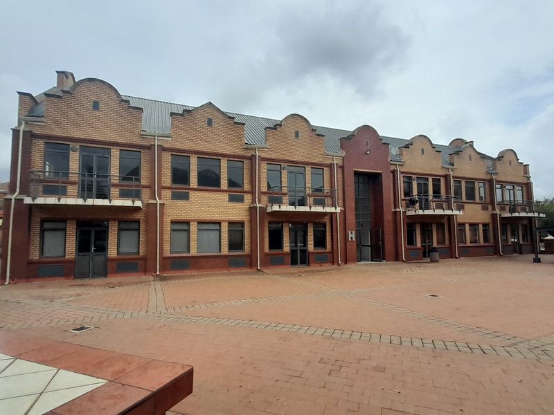 A multi-story office building featuring a brick facade, multiple balconies, and a large paved courtyard area.