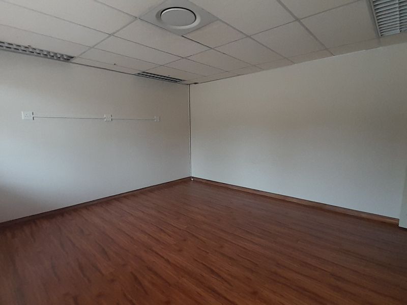 A vacant office space featuring laminate flooring, a suspended ceiling with recessed lighting, and surface-mounted electrical trunking along the walls.