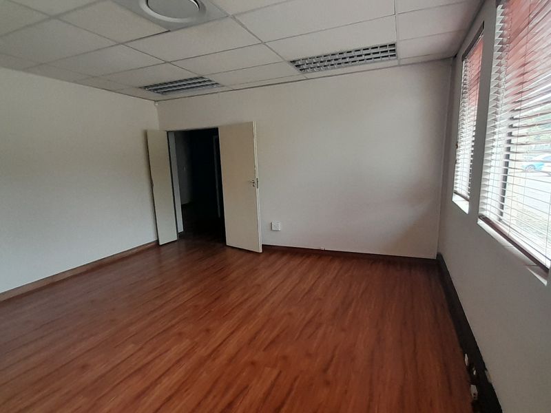 A vacant office space featuring laminate flooring, a suspended ceiling with recessed lighting, and large windows fitted with venetian blinds.