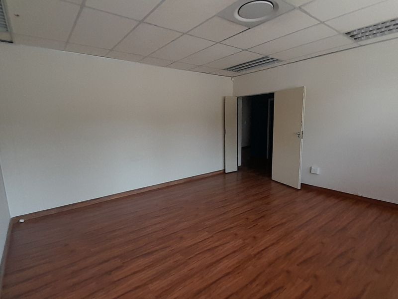 A vacant office space featuring laminate flooring, a suspended ceiling with recessed lighting, and double door access.
