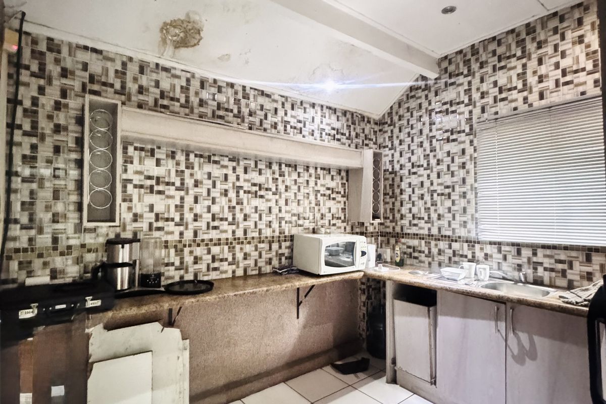 A dated kitchen area featuring tiled walls, built-in cabinetry, a stainless steel sink, and visible ceiling water damage requiring repair.