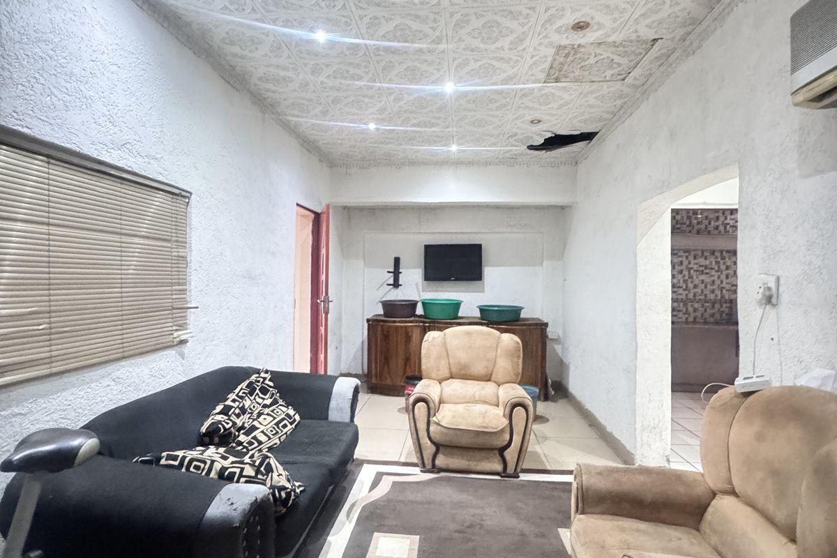 A living room area featuring textured walls, a decorative ceiling, and recessed lighting, with an adjacent kitchen space visible through the doorway.