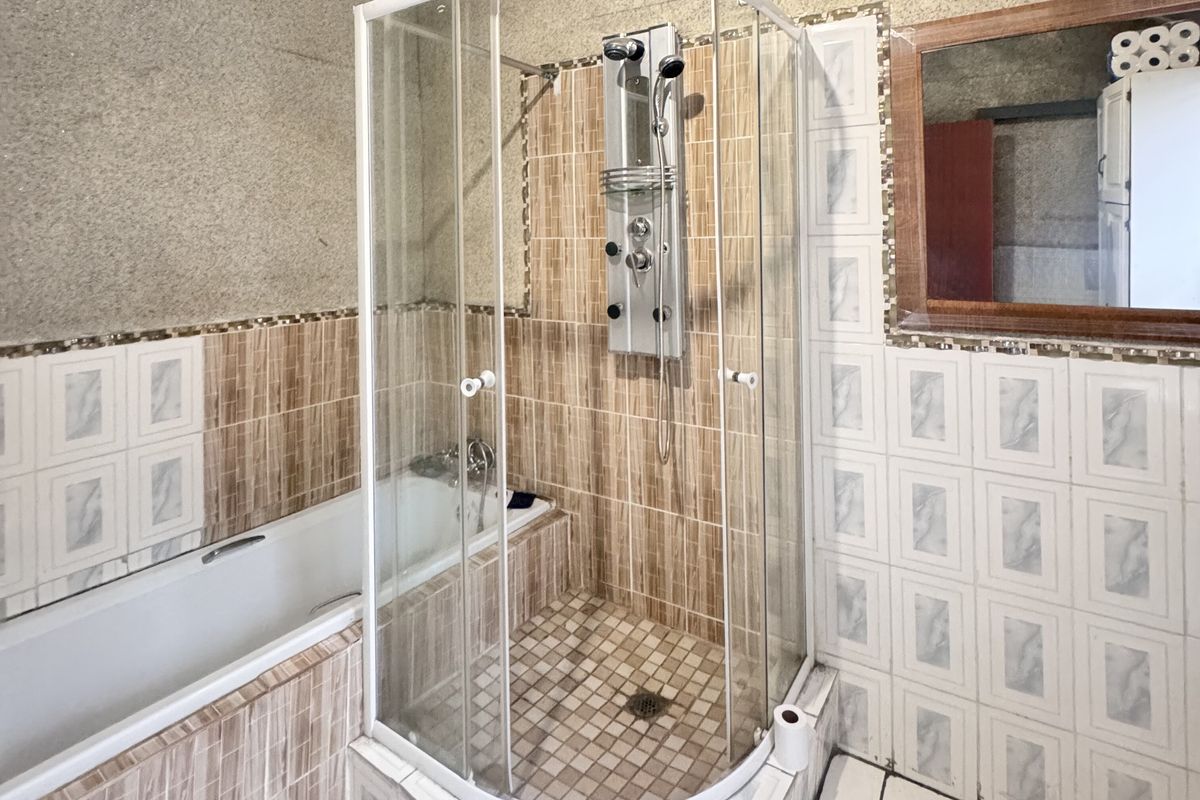 A functional bathroom featuring a built-in bathtub and a separate corner shower enclosure with a modern shower panel system.