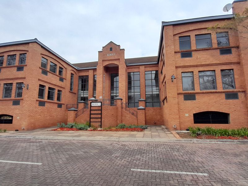 A professional exterior view of a multi-story brick office building featuring a paved driveway and landscaped entrance area.