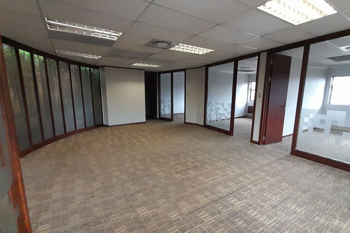 Spacious, vacant office area featuring glass partitions, suspended ceilings with recessed lighting, and carpeted flooring, offering a flexible layout for professional use.