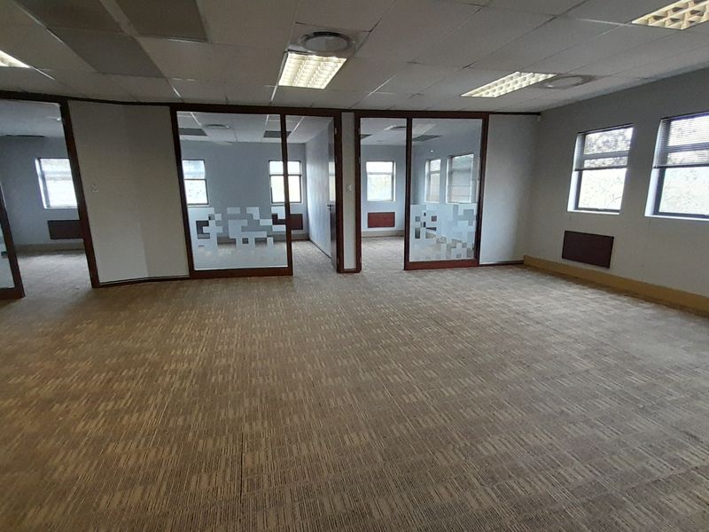 An open-plan office space featuring glass partitions, suspended ceilings with recessed lighting, and carpeted flooring, offering a versatile layout for professional use.