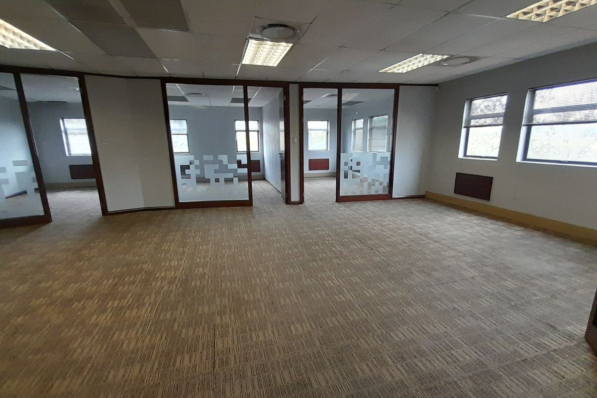An open-plan office space featuring glass partitions, suspended ceilings with recessed lighting, and carpeted flooring, offering a versatile layout for professional use.
