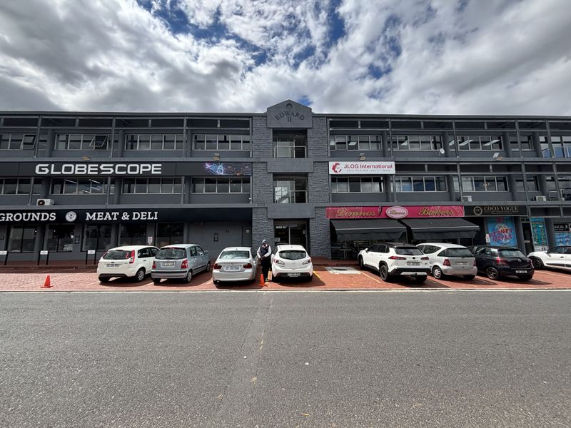 Front elevation of a multi-story commercial office building featuring ground-floor retail units, paved parking, and prominent signage.
