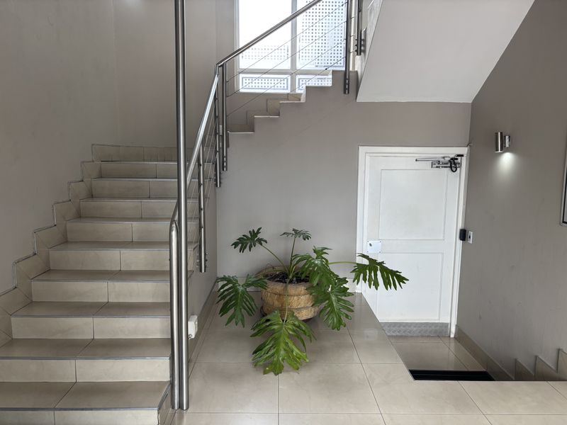 A clean and well-maintained office hallway featuring a tiled staircase with a modern stainless steel balustrade and a secure fire door.