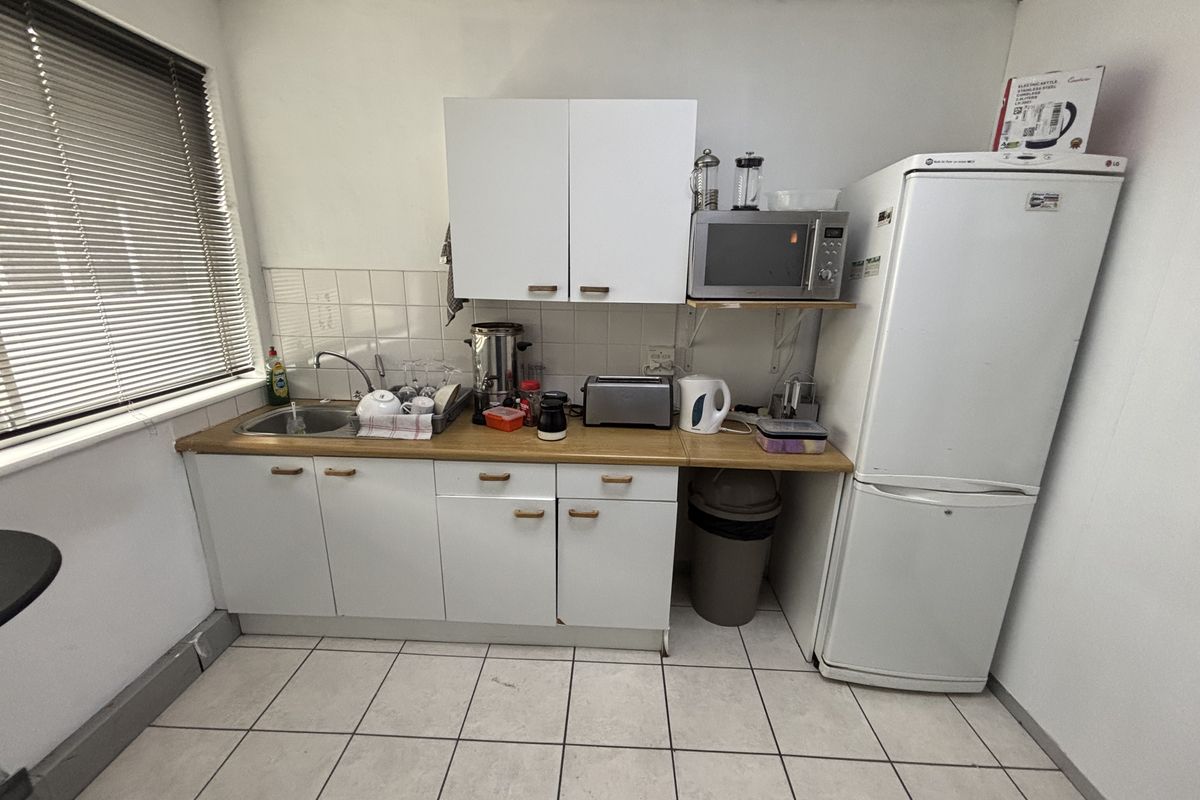 A functional office kitchenette featuring white cabinetry, a laminate countertop, stainless steel sink, and tiled flooring.