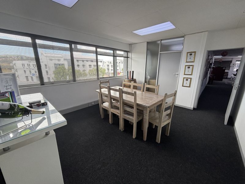 A bright office space featuring large windows with venetian blinds, recessed ceiling lighting, and a glass partition wall, providing a professional work environment.