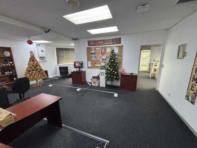 A functional office space featuring carpeted flooring, recessed lighting, and built-in shelving, with an adjacent room visible through the doorway.