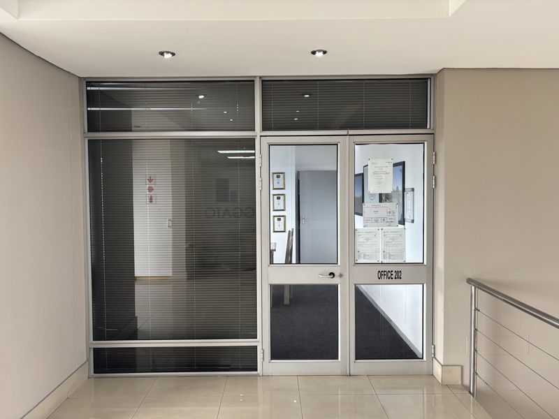 Entrance to Office 202 featuring a modern aluminium and glass door system with integrated sidelight, venetian blinds, and professional tiled hallway access.