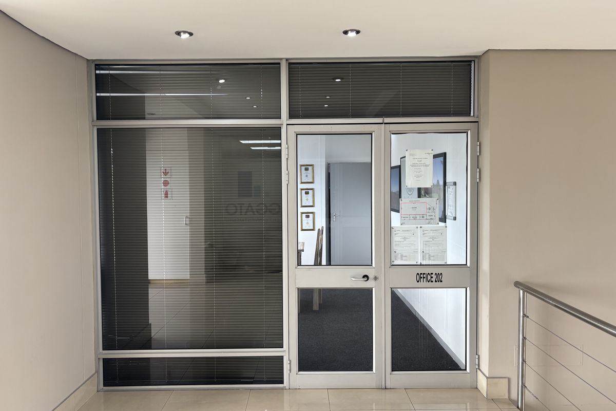 Entrance to Office 202 featuring a modern aluminium and glass door system with integrated sidelight, venetian blinds, and professional tiled hallway access.