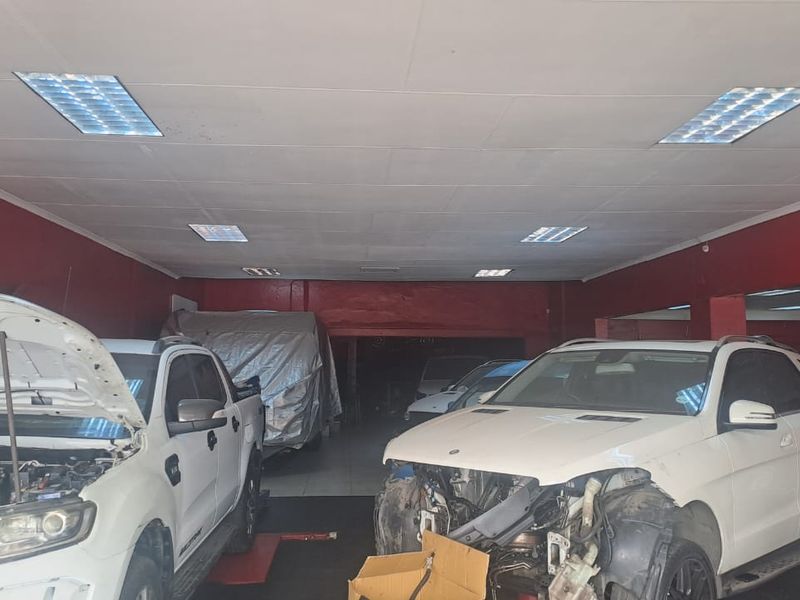 A spacious commercial workshop area featuring recessed ceiling lighting and red painted walls, currently utilized for vehicle maintenance and repair services.