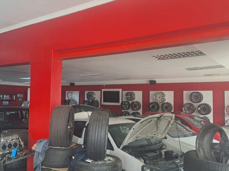 Spacious retail workshop area featuring open-plan layout, drop ceiling with integrated lighting, and prominent structural pillars, currently utilized for automotive display and service.