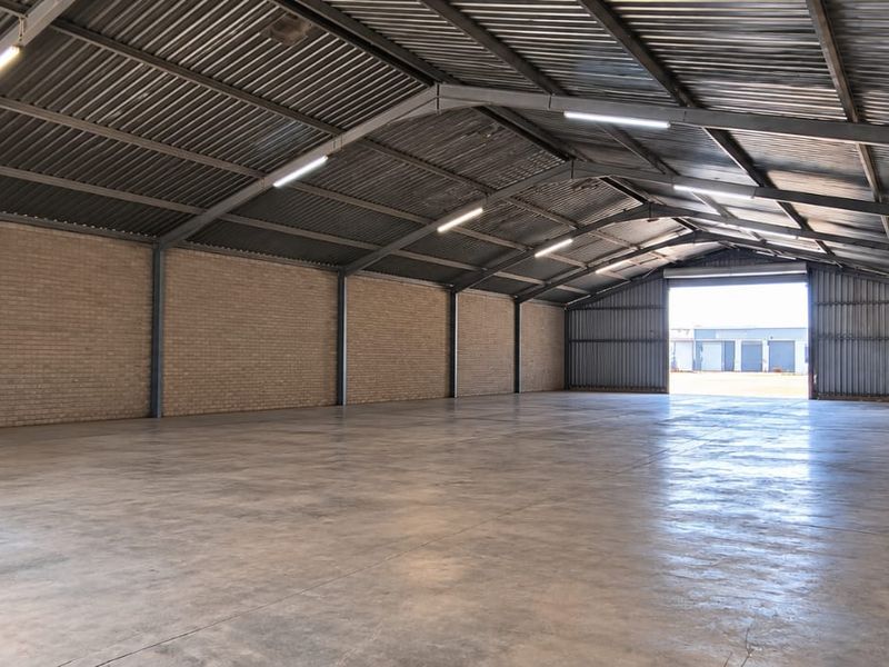 Spacious industrial warehouse featuring a steel portal frame, concrete flooring, brick walls, and high-clearance corrugated metal roofing with integrated lighting.