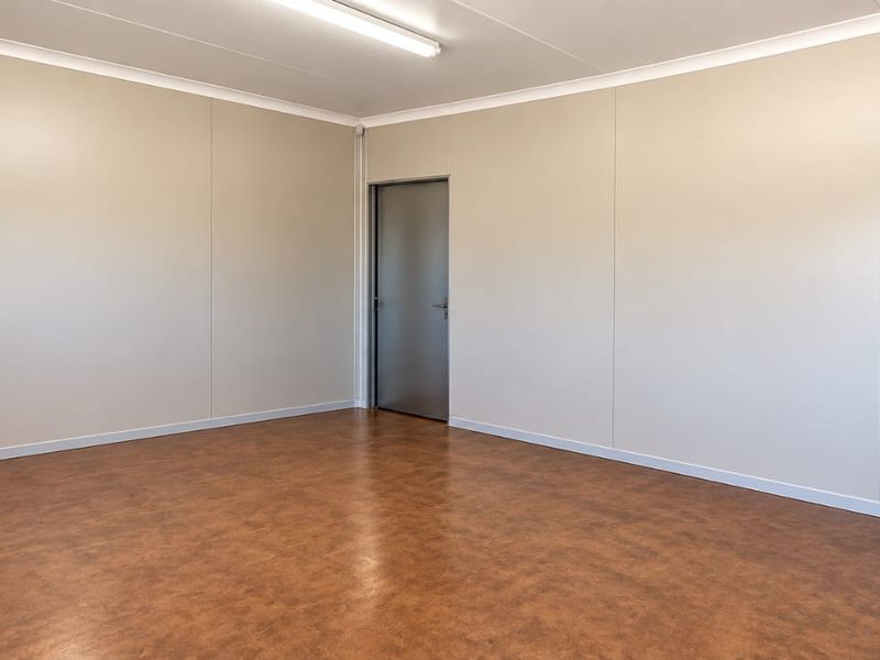 A clean, empty office space featuring neutral wall panels, durable vinyl flooring, and efficient overhead fluorescent lighting.