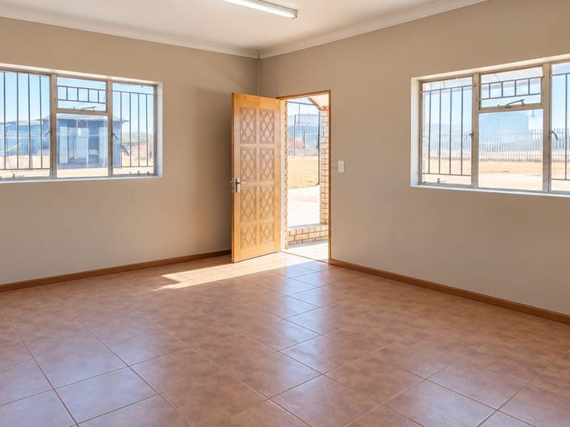 A clean, empty office space featuring tiled flooring, security bars on windows, and a timber entrance door, suitable for various industrial or commercial uses.