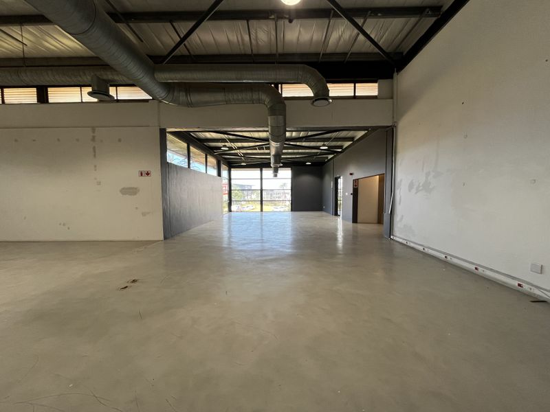 Spacious open-plan retail unit featuring high exposed ceilings, industrial ducting, polished concrete flooring, and large windows providing ample natural light.