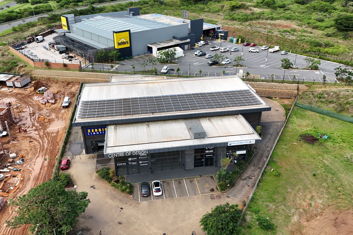 Aerial view of a modern retail complex featuring a large warehouse building, paved parking areas, and solar panel installations on the roof.