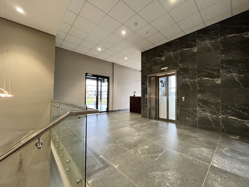 Modern commercial lobby featuring polished marble-look floor tiles, a feature marble wall, glass balustrade, and a built-in elevator access point.