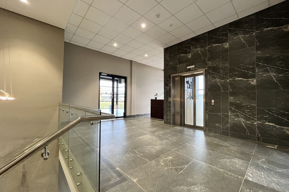Modern commercial lobby featuring polished marble-look floor tiles, a feature marble wall, glass balustrade, and a built-in elevator access point.