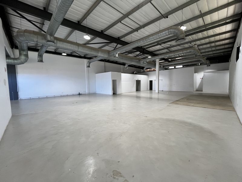 Spacious open-plan retail or industrial unit featuring high exposed ceilings, industrial ducting, polished concrete floors, and multiple internal access points.
