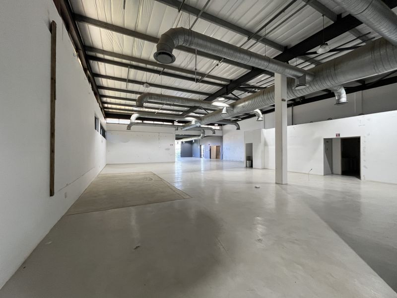 Spacious open-plan retail or industrial unit featuring high exposed ceilings, industrial ducting, polished concrete flooring, and neutral white walls.