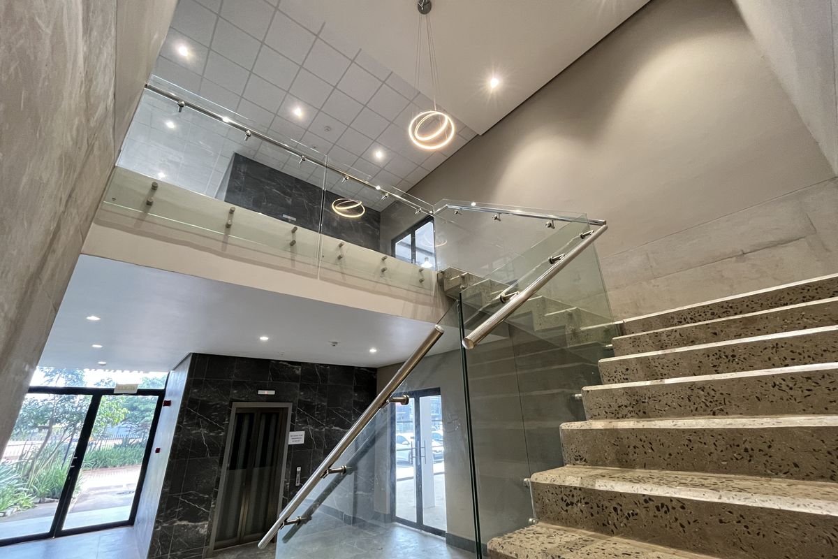 Modern commercial lobby featuring a striking terrazzo staircase, glass balustrades, marble-look wall cladding, and contemporary pendant lighting.