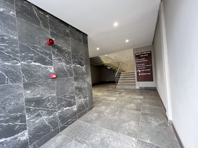 Modern commercial building entrance lobby featuring marble-look tiled flooring, wall cladding, and a glass-railed staircase leading to the first floor.