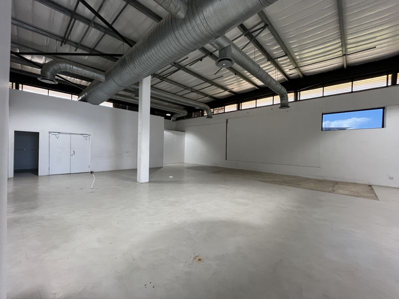 Spacious open-plan retail or industrial unit featuring high exposed ceilings, industrial ducting, polished concrete floors, and ample natural light through clerestory windows.