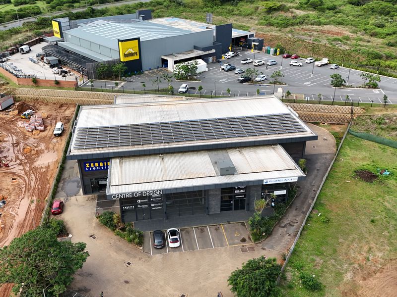 Aerial view of a modern retail complex featuring a large warehouse building, paved parking areas, and solar panel installations on the roof.