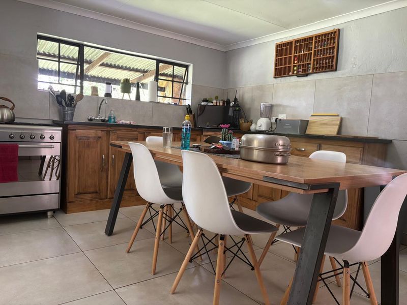 Open-plan kitchen and dining area featuring wooden cabinetry, a stainless steel gas stove, tiled backsplash, and neutral floor tiles.
