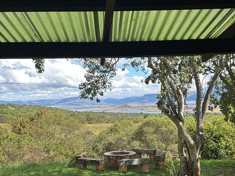 A covered outdoor patio area featuring a corrugated metal roof and timber beams, overlooking a scenic landscape with distant mountains and water.