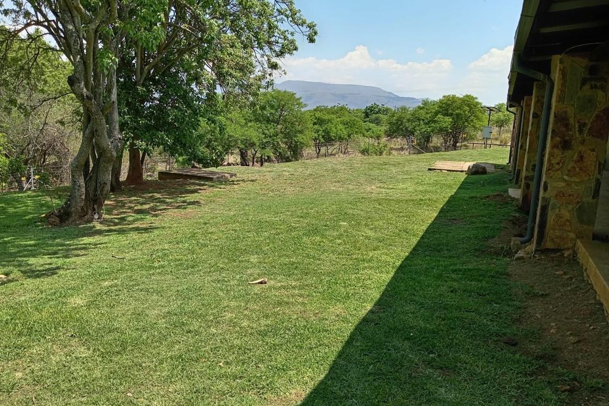 A spacious rear garden area featuring natural stone wall cladding on the building exterior, established trees, and scenic mountain views.